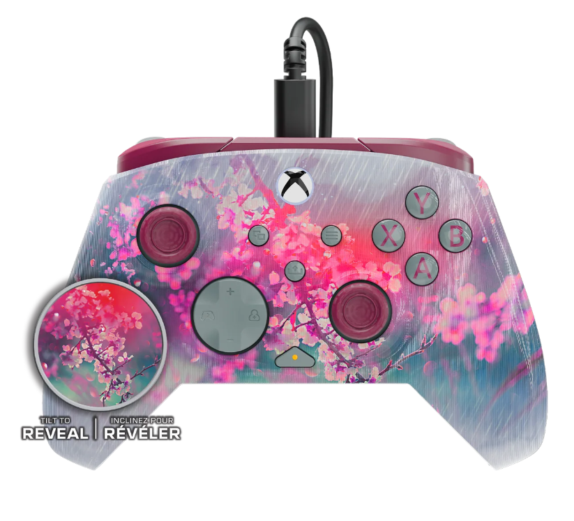 Kontroler Xbox z kwiatowym wzorem. Różowe i fioletowe kwiaty na szarym tle. Przyciski są kolorowe i oznaczone.