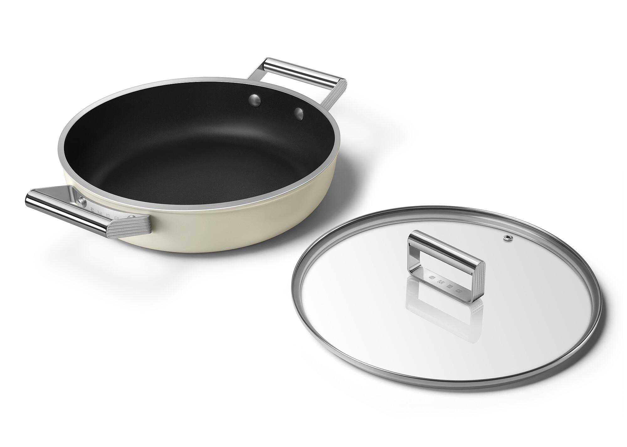 Cremefarbene Pfanne mit schwarzem Innenraum und Glasdeckel mit Metallgriff. Der Deckel liegt neben der Pfanne auf weißem Untergrund.