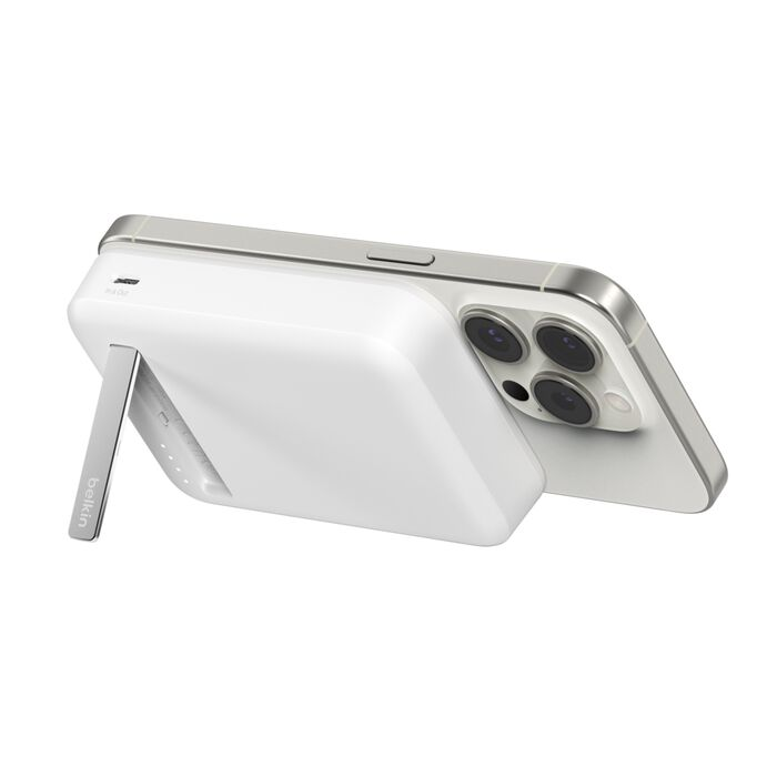 Un cargador MagSafe Belkin blanco con un iPhone. El teléfono es plateado y tiene tres lentes de cámara. El cargador tiene un soporte.