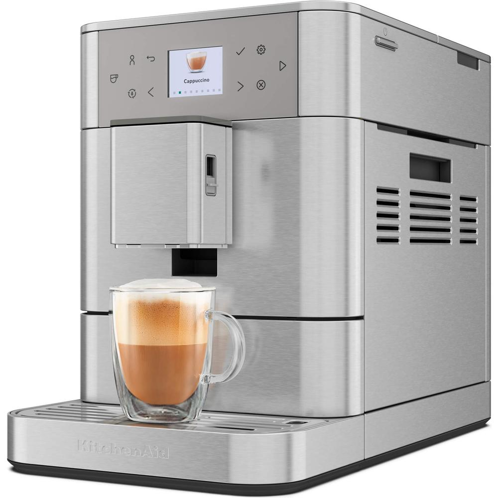 Una máquina de espresso KitchenAid plateada con pantalla de capuchino y un vaso de capuchino delante.