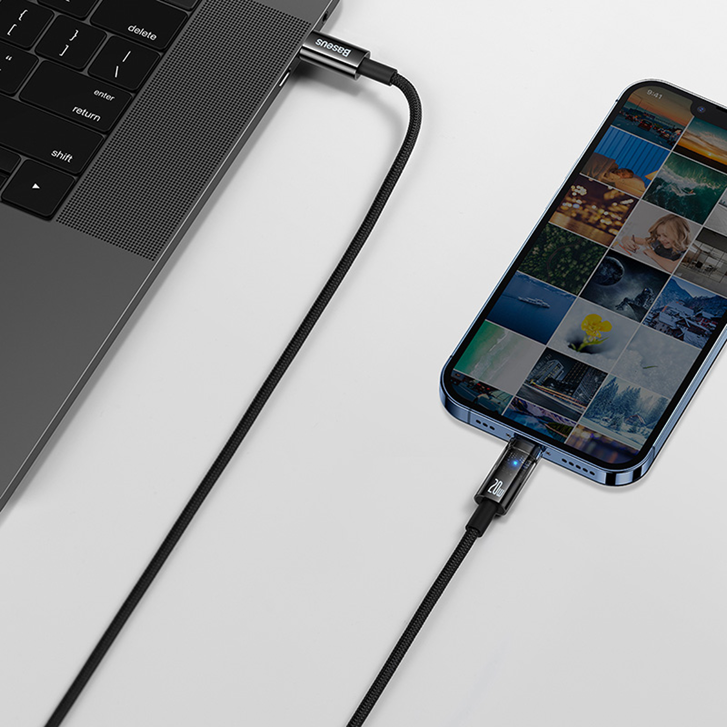 Un teléfono está conectado a una computadora portátil con un cable de carga negro. El teléfono muestra fotos. El cable tiene un indicador de '20W'.