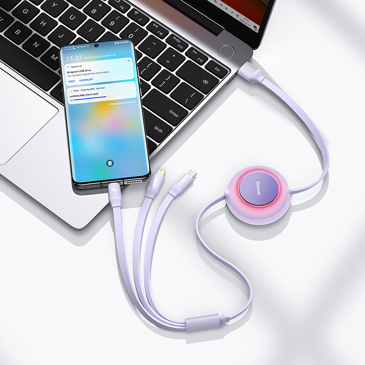 Un teléfono está conectado a un portátil mediante un cable de carga morado. También hay un cargador conectado. El teléfono muestra notificaciones.