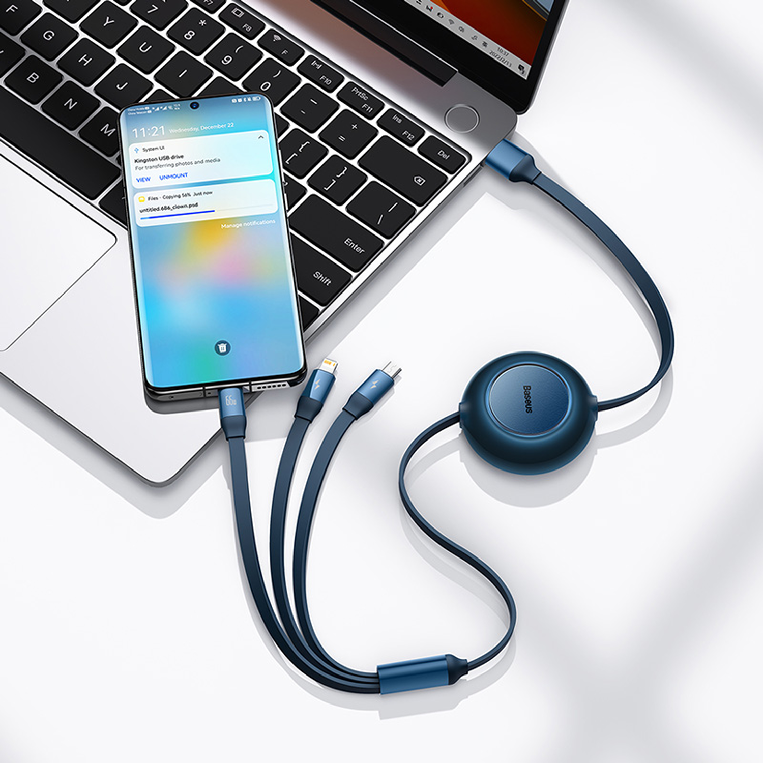 Un teléfono conectado a una laptop mediante un cable de carga azul. El teléfono muestra notificaciones. Un organizador de cables Baseus es visible.