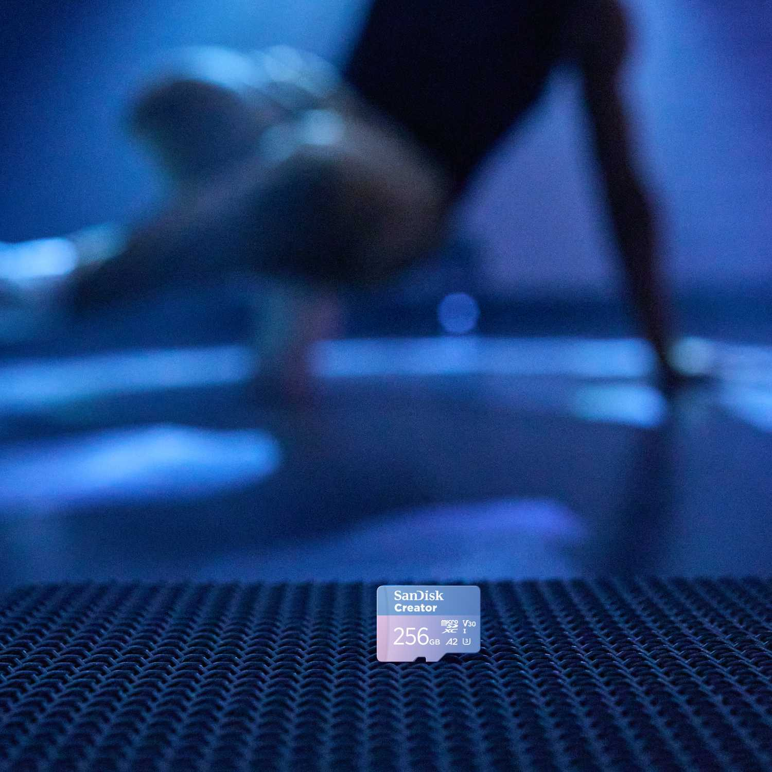 Una tarjeta micro SD sobre una superficie texturizada. Un bailarín borroso en el fondo, iluminación azul.