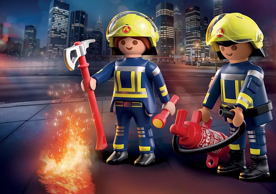 Zwei Spielzeugfeuerwehrleute in blauen Uniformen mit gelben Helmen. Einer hält eine Axt, der andere einen Feuerlöscher. Skyline im Hintergrund.