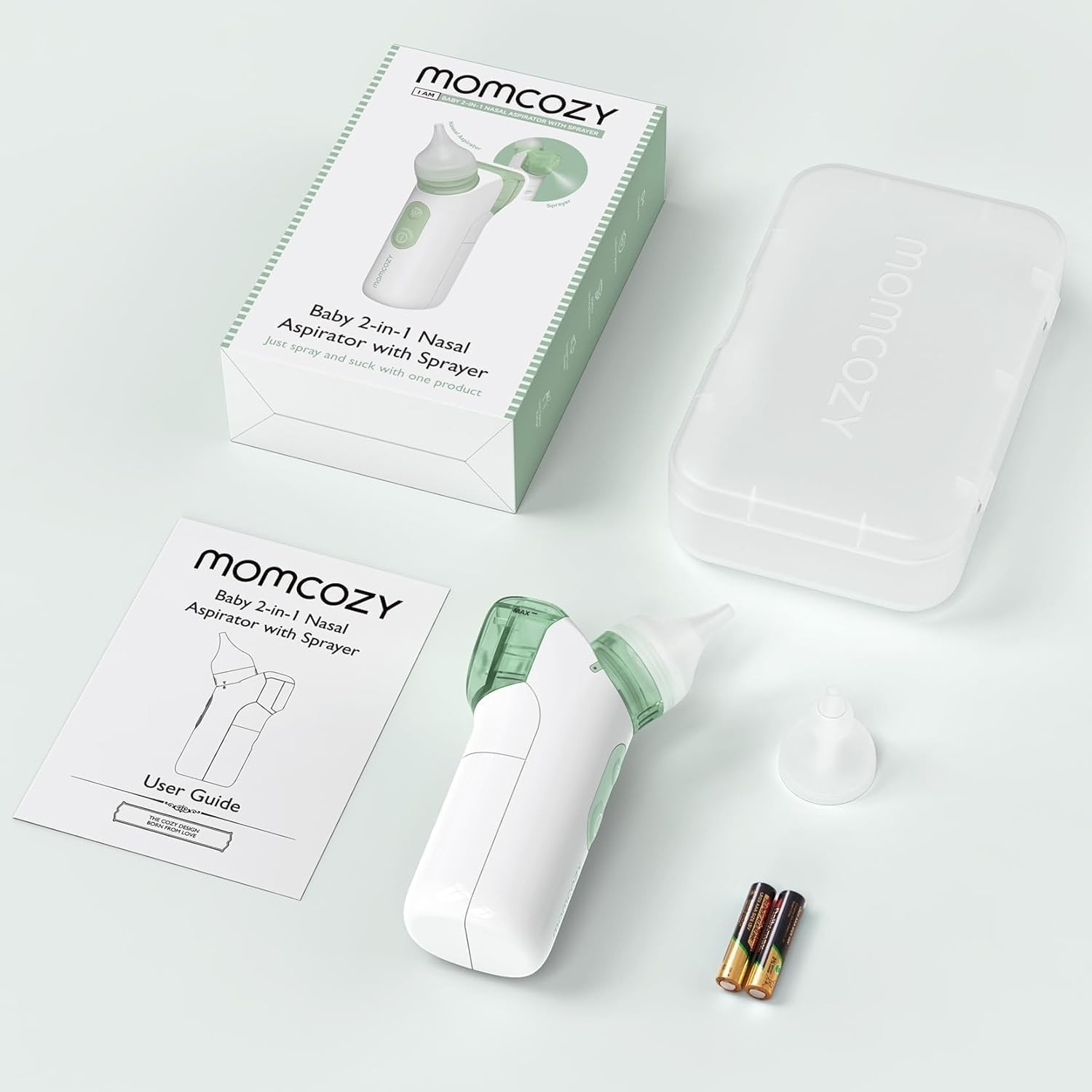 Un aspiratore nasale per bambini Momcozy bianco e verde, scatola, custodia, guida utente, batterie e ugello su una superficie bianca.
