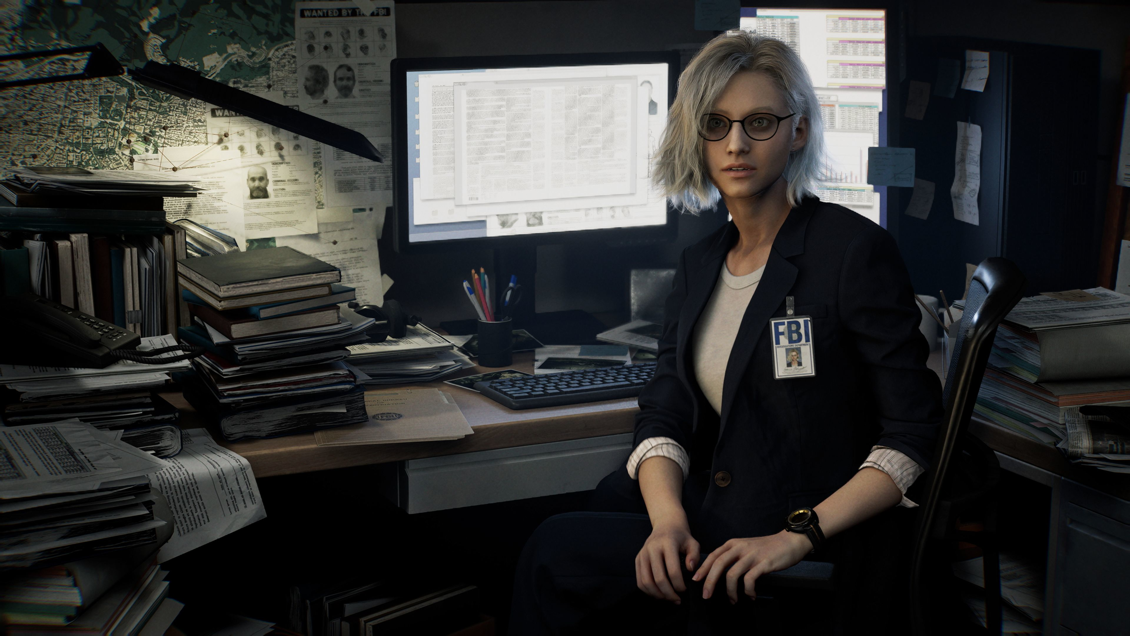 Eine FBI-Agentin mit Brille sitzt an einem überfüllten Schreibtisch. Akten, ein Computer und ein Fahndungsplakat füllen den Hintergrund.