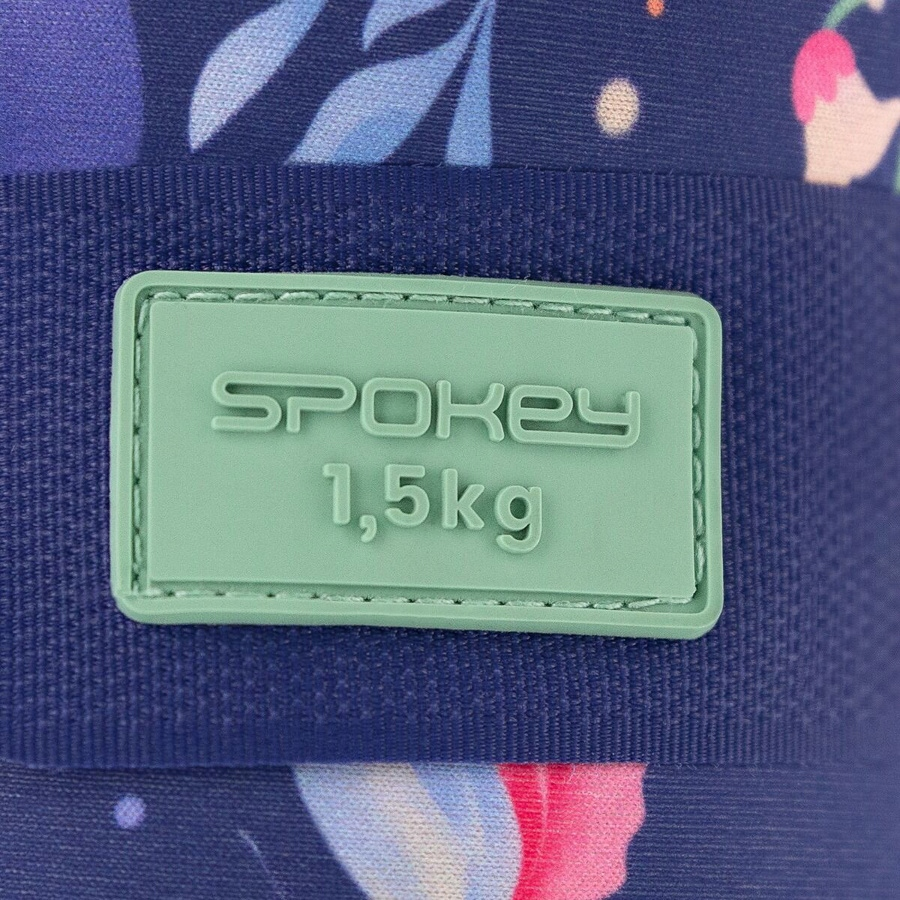 Zbliżenie torby z zieloną etykietą. Etykieta głosi 'SPOKEY 1,5kg'. Tło ma wzory kwiatowe i ciemnoniebieski pasek.