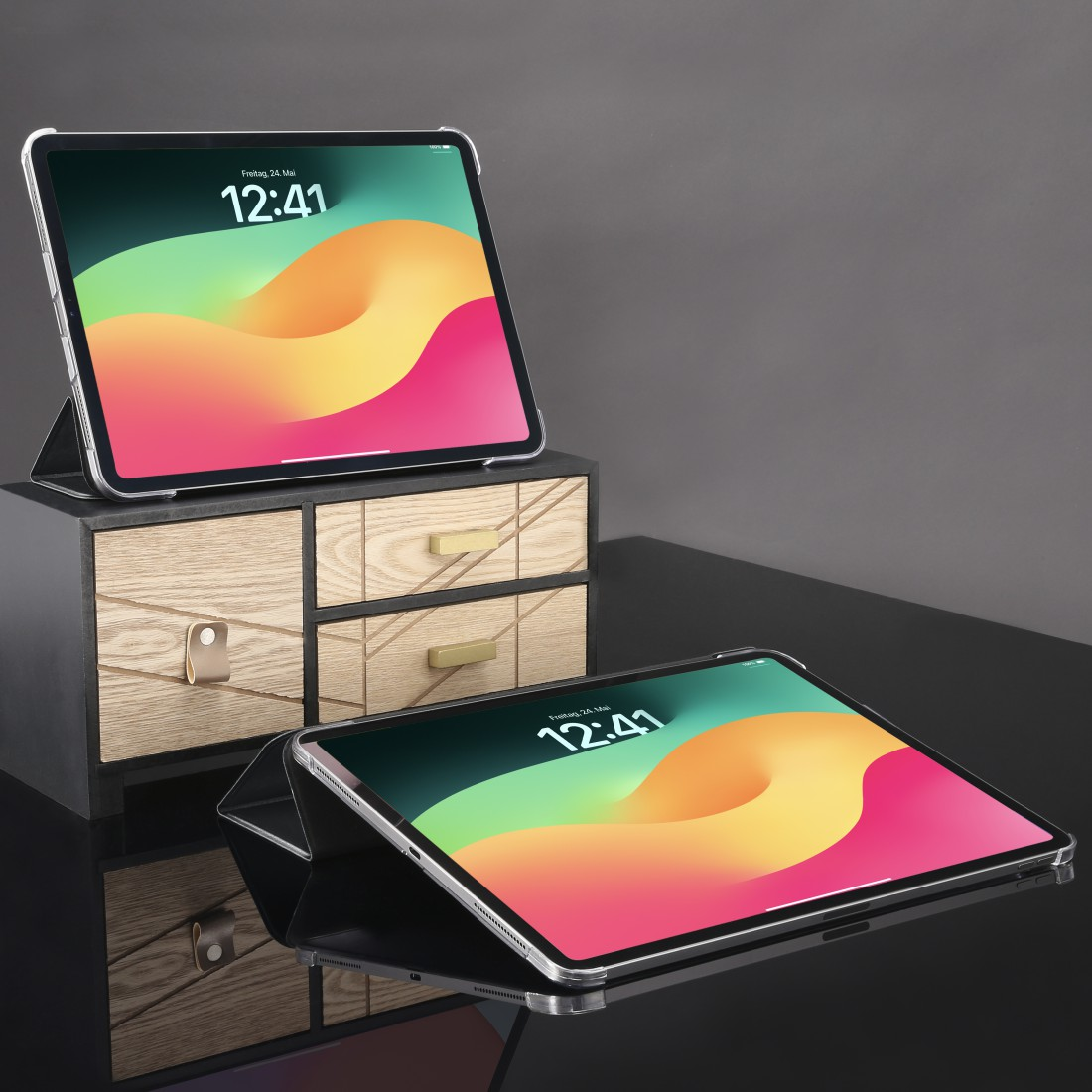Zwei iPads mit bunten Bildschirmen. Eines liegt auf einer Holzkommode, das andere auf einer reflektierenden Oberfläche.
