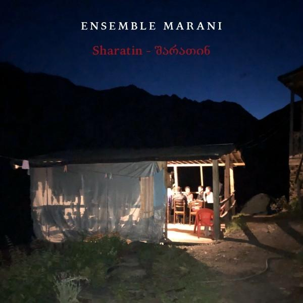 Nachtszenario. Eine überdachte Veranda mit Personen, die an einem Tisch sitzen. Berge im Hintergrund. Text: Ensemble Marani, Sharatim.