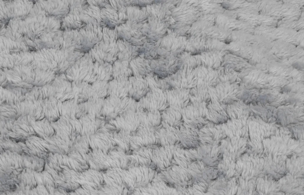 Zbliżenie miękkiej, szarej, puszystej tkaniny. Tekstura wydaje się gęsta z wieloma małymi, zaokrąglonymi kępkami.