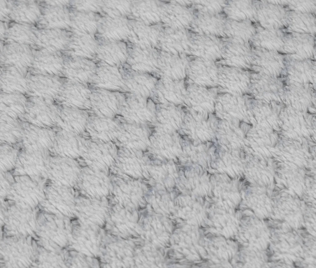 Zbliżenie miękkiej, teksturowanej tkaniny. Tkanina jest jasnoszara z wzorem małych, wypukłych wypukłości.