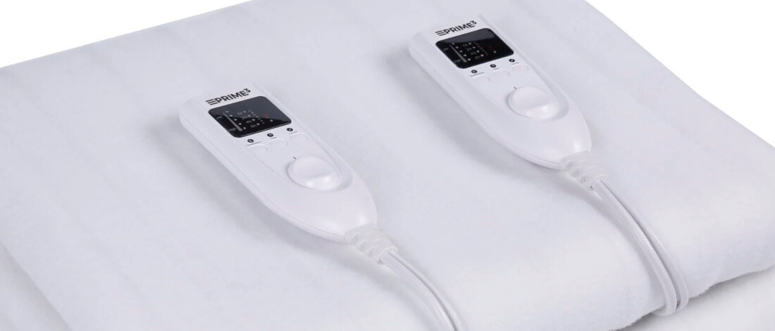 Dwa białe kontrolery do koców elektrycznych na białym kocu. Każdy kontroler ma wyświetlacz i przyciski.