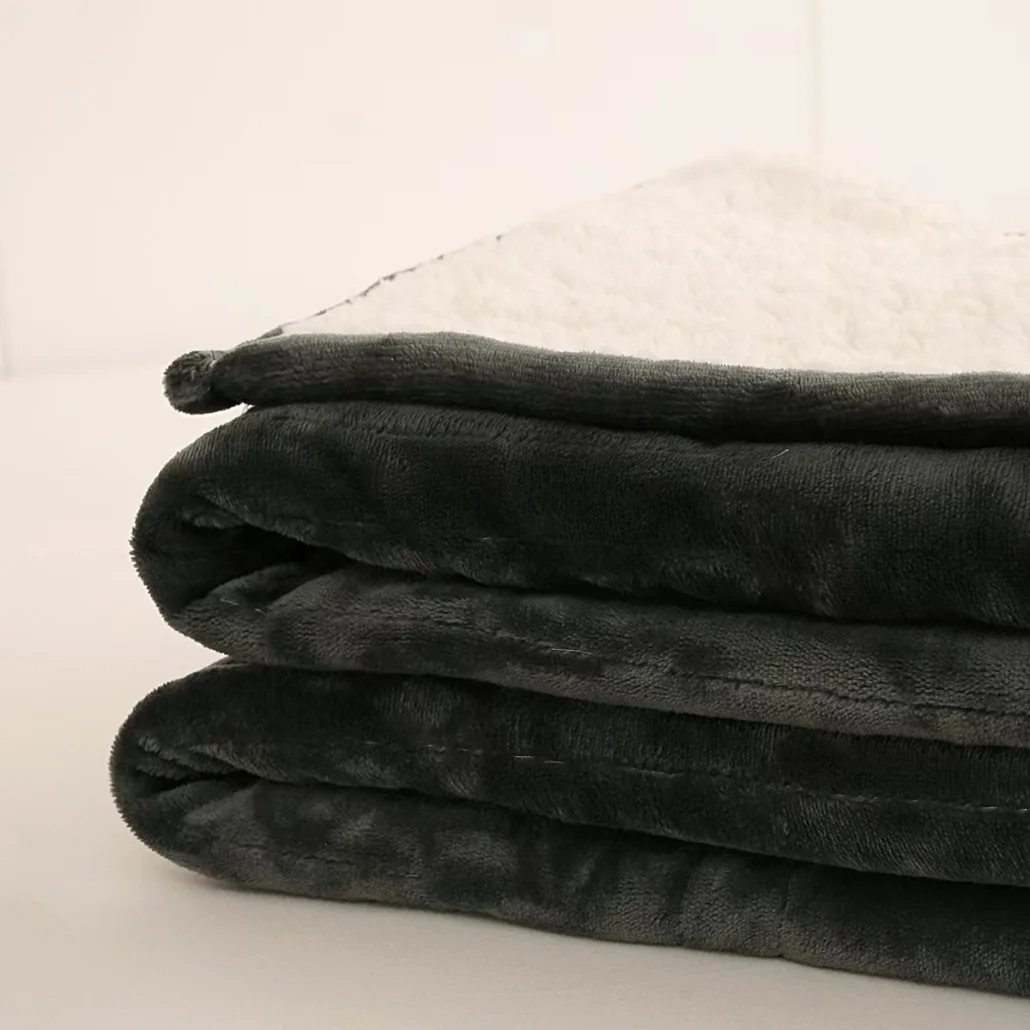 Złożony koc z ciemnoszarym zewnętrzem i białym, puszystym wnętrzem. Warstwy są widoczne. Tło jest białe.