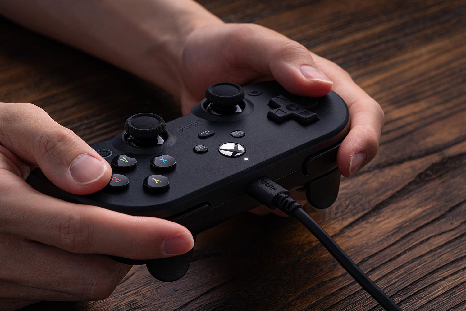Hände halten einen schwarzen Gamecontroller. Knöpfe sind A, B, X, Y. Der Controller ist mit einem Kabel verbunden.