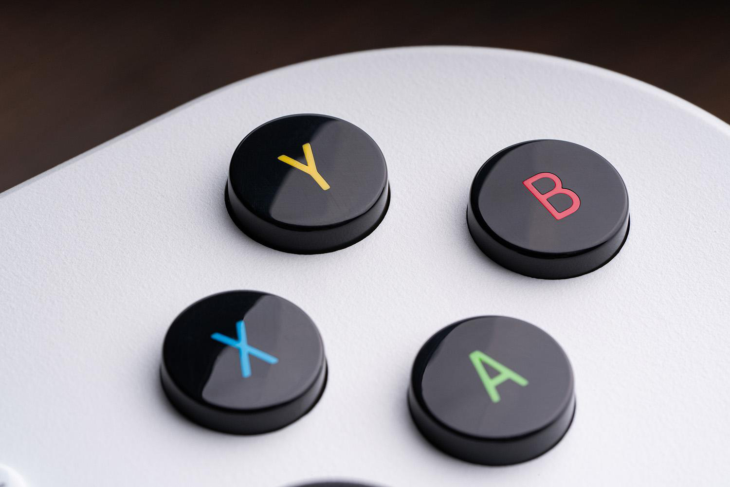 Nahaufnahme eines Gamecontrollers. Vier schwarze Knöpfe mit farbigen Buchstaben: Y(gelb), B(rot), X(blau) und A(grün) auf weißer Oberfläche.