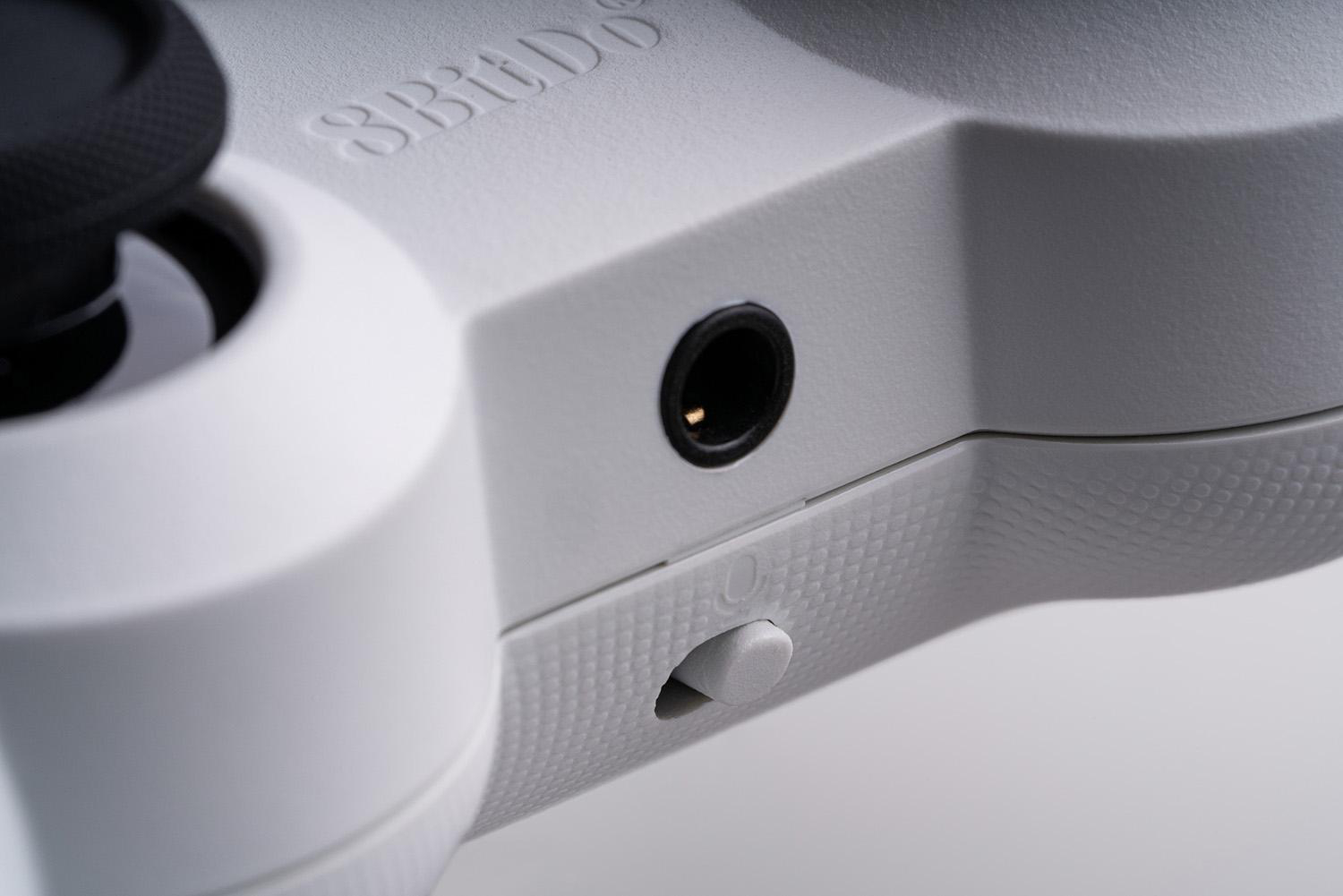 Nahaufnahme eines weißen Gamecontrollers. Links befindet sich ein schwarzer Joystick. Rechts sind ein Anschluss und ein Schalter zu sehen.