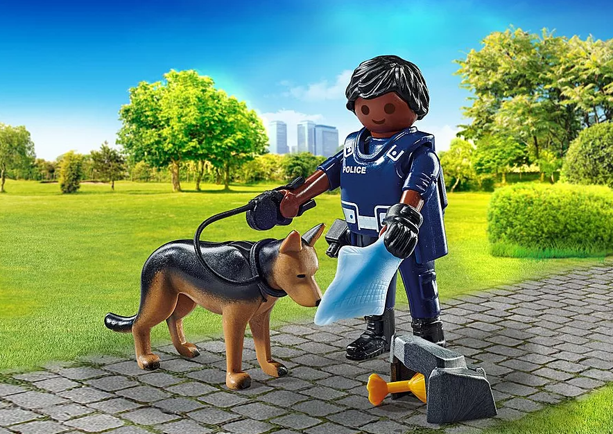 Ein Polizist mit einem Schäferhund in einem Park. Der Polizist hält eine Leine und eine blaue Tüte. Auch eine Hundekotentsorgungseinheit ist vorhanden.