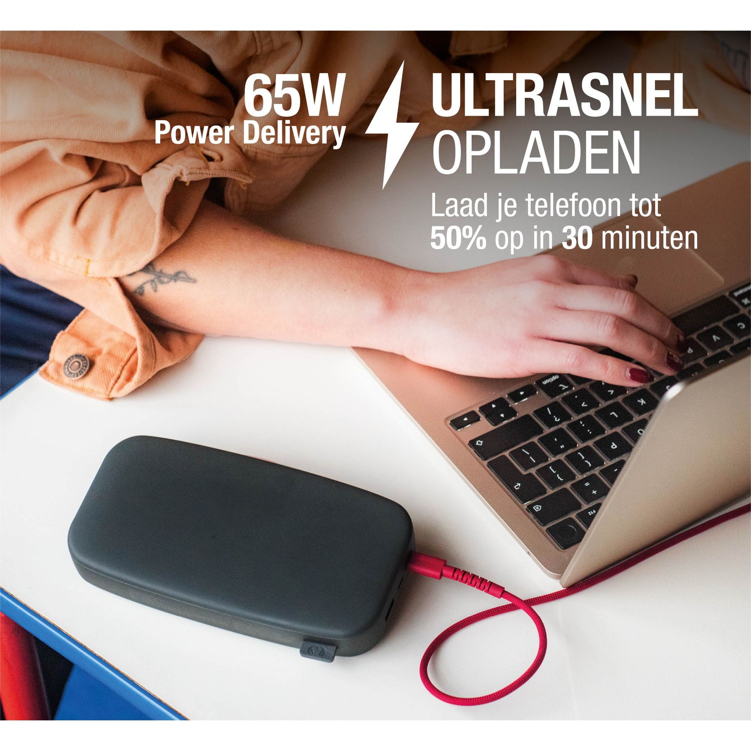 Een persoon gebruikt een laptop terwijl hij een zwarte powerbank oplaadt met een rode kabel. Tekst: '65W Power Delivery' en 'Ultrasnel Opladen'.