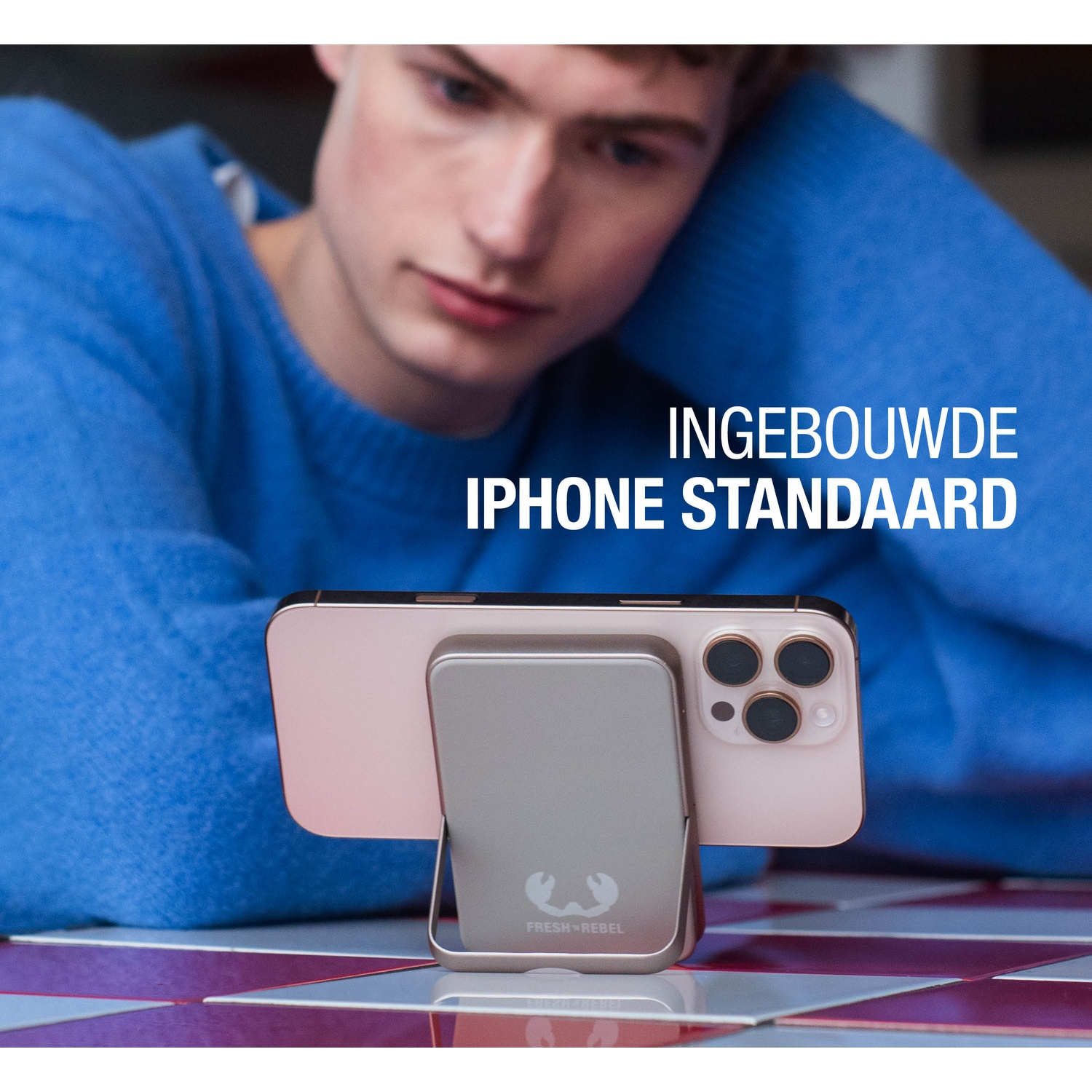 A man looks at his phone, which is in a stand. The phone is pink and has three cameras. The stand is gray.