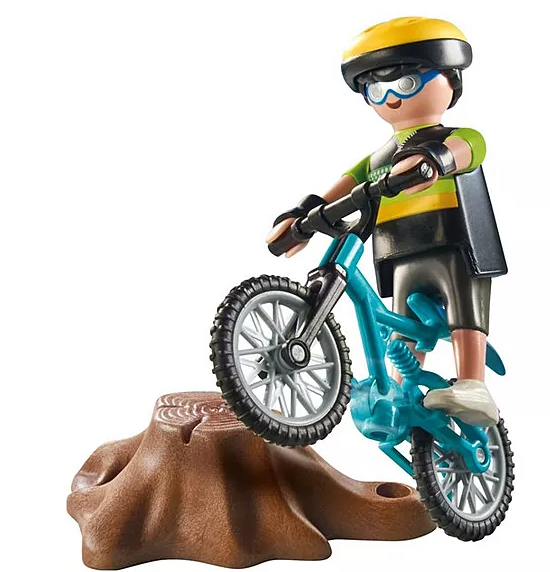 Eine Spielfigur auf einem blauen Fahrrad. Die Figur trägt einen gelben Helm, eine Brille und schwarze Shorts. Das Fahrrad steht über einem braunen Baumstumpf.