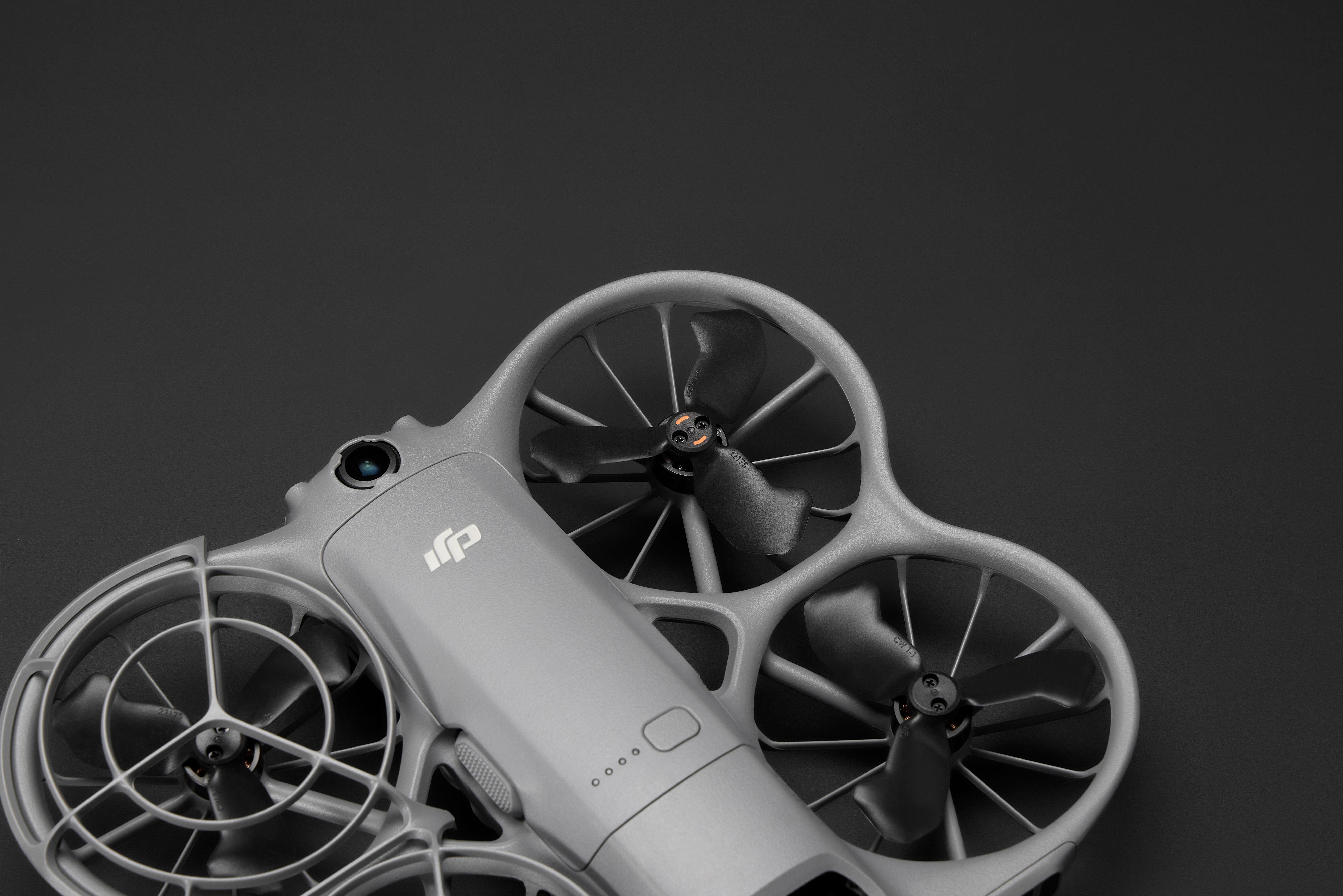 Eine graue Drohne mit schwarzen Propellern auf dunklem grauem Hintergrund. Die Drohne hat eine Kamera und ein DJI-Logo.