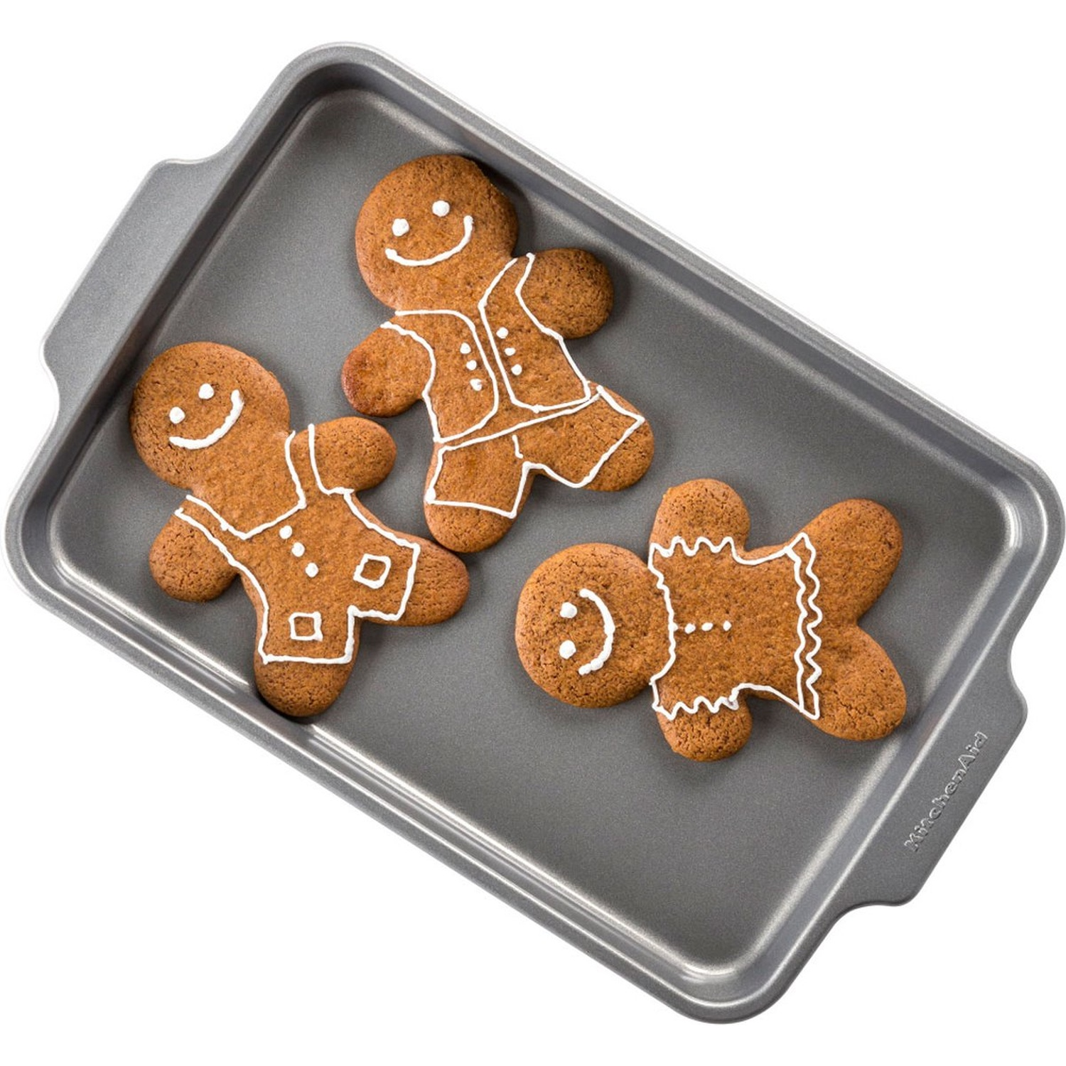 Trois biscuits bonhommes en pain d'épices sur une plaque de cuisson grise. Chaque biscuit a des détails de glaçage blanc et un visage souriant.