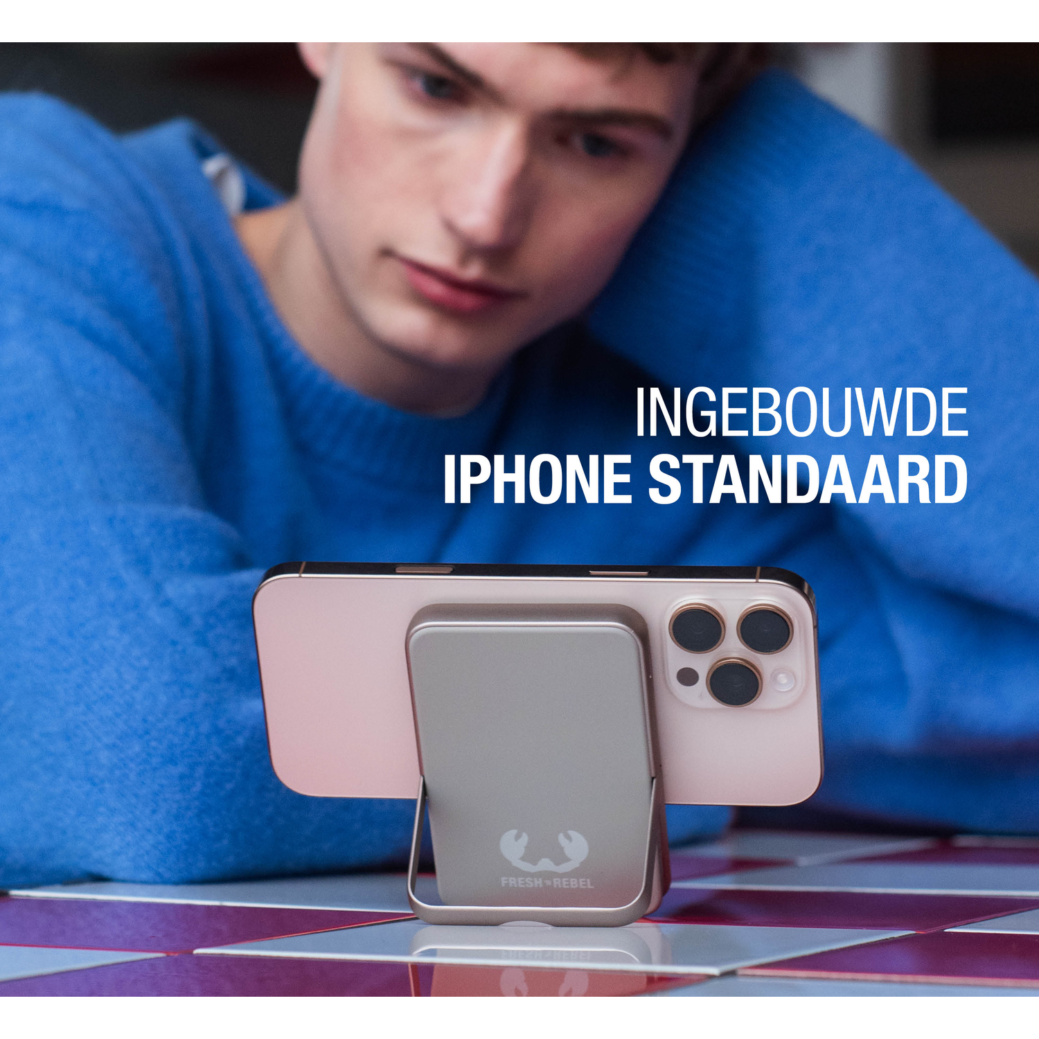 A person looks at a phone on a stand. The stand is holding a pink phone. The background is a blue sweater and a checkered table.