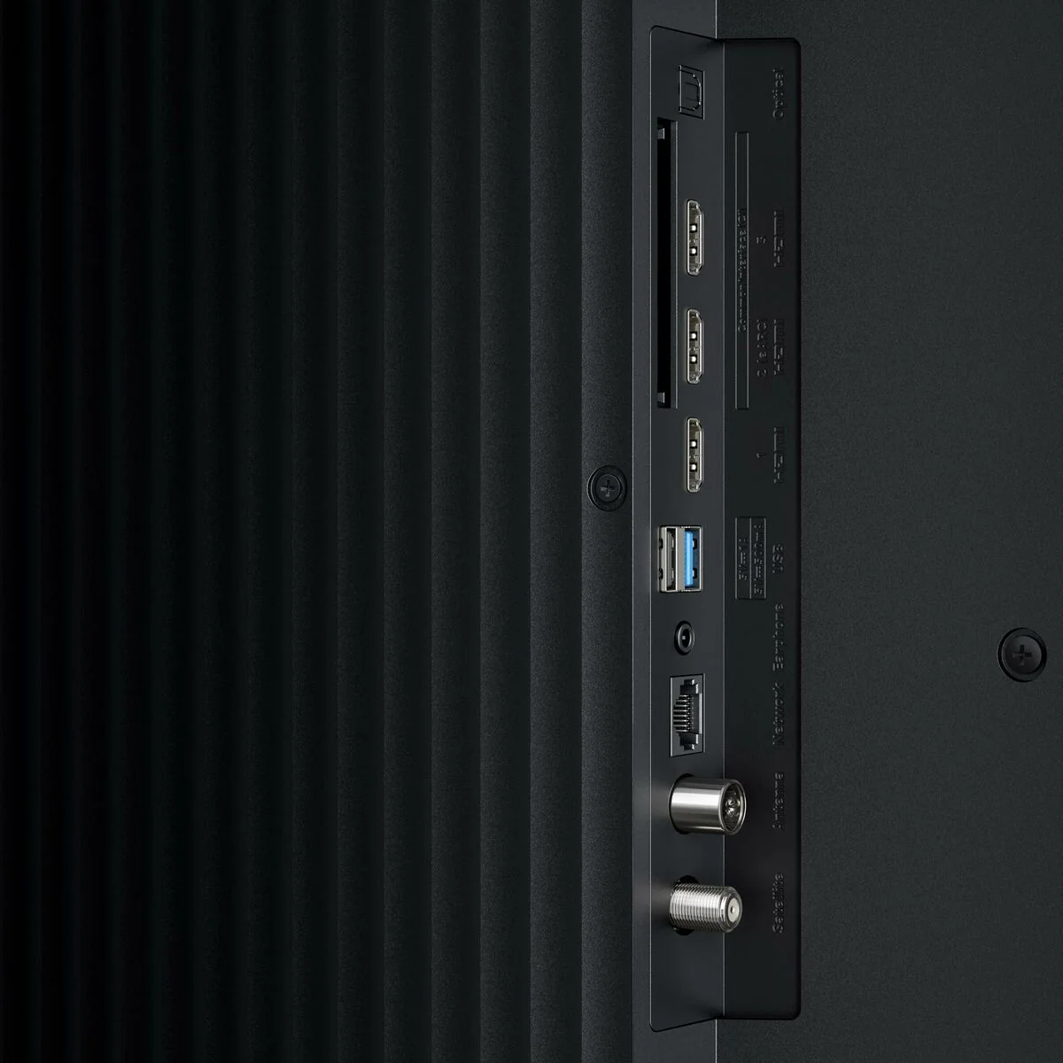 A TV hátlapjának közeli képe. Különböző portokat tartalmaz: HDMI, USB, Ethernet, antenna és műholdas csatlakozásokat. A panel fekete.