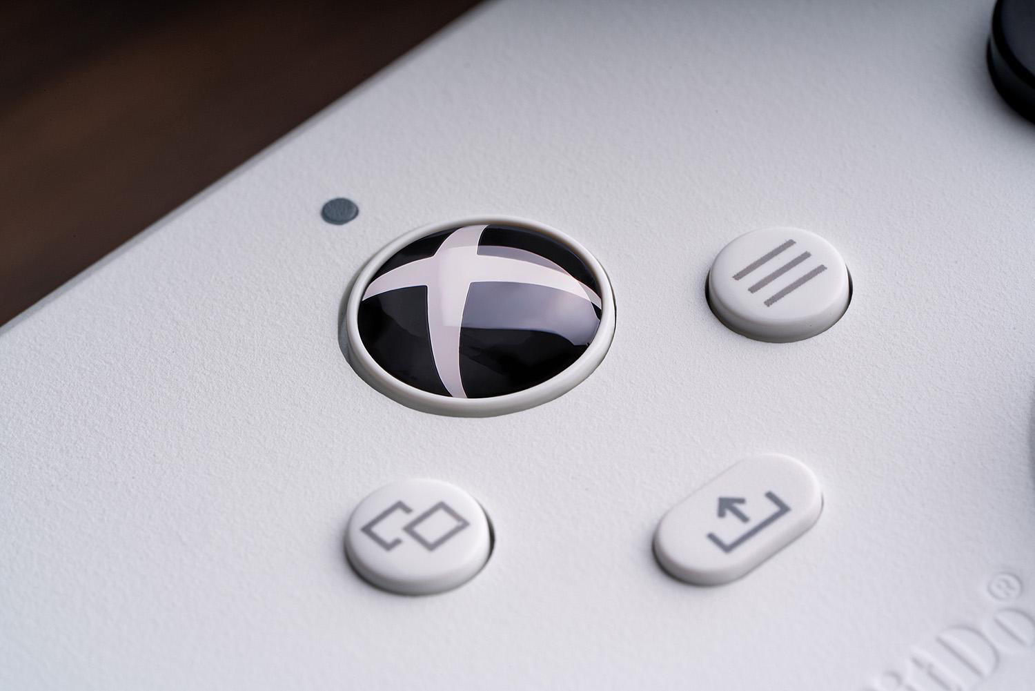 Nahaufnahme eines weißen Gamecontrollers. Eine schwarze Taste mit weißem X-Logo ist prominent. Andere Tasten sind sichtbar.