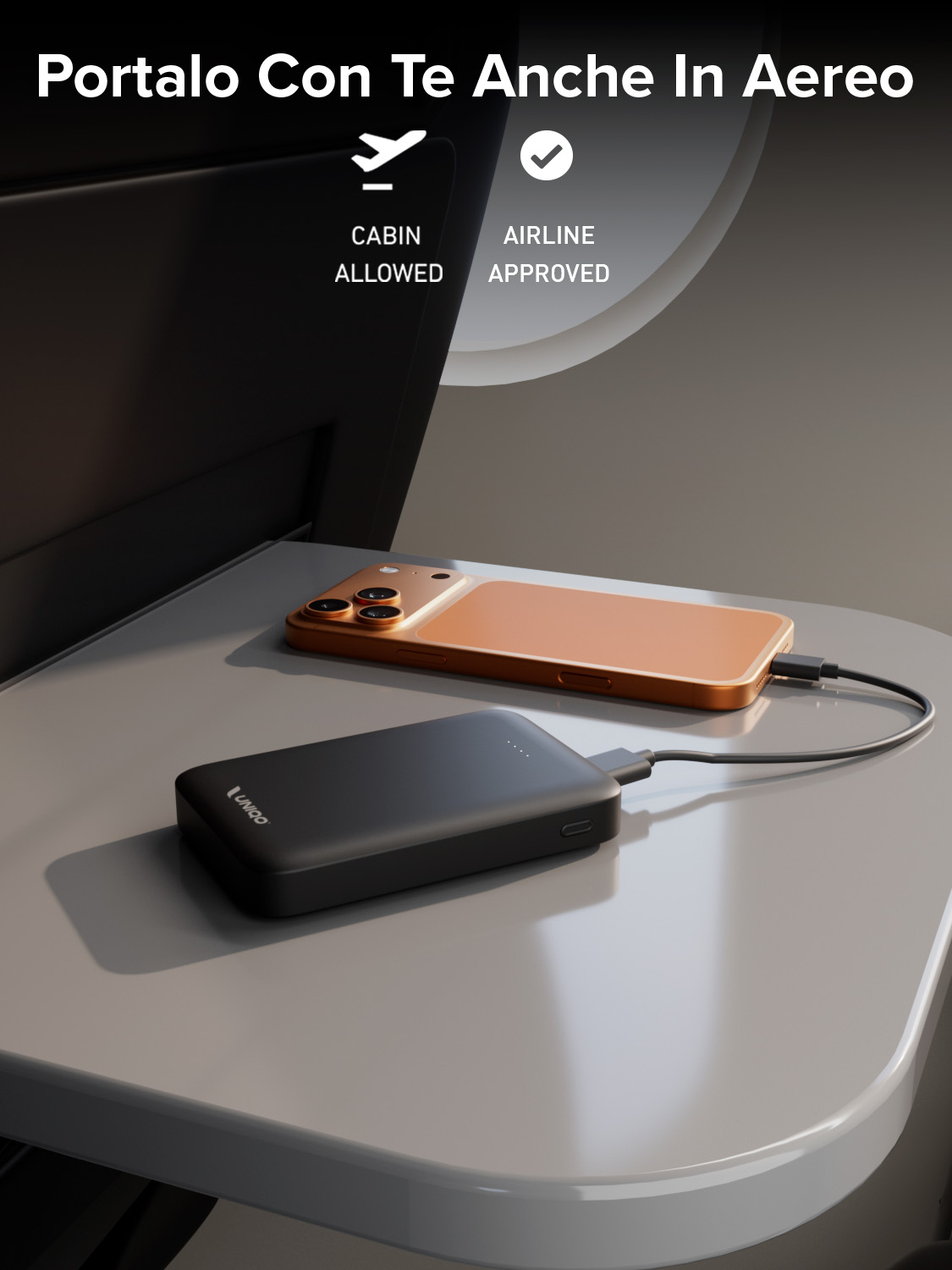 Un telefono si ricarica su un tavolino dell'aereo con un power bank. Il testo indica che è approvato per la cabina e dalla compagnia aerea.