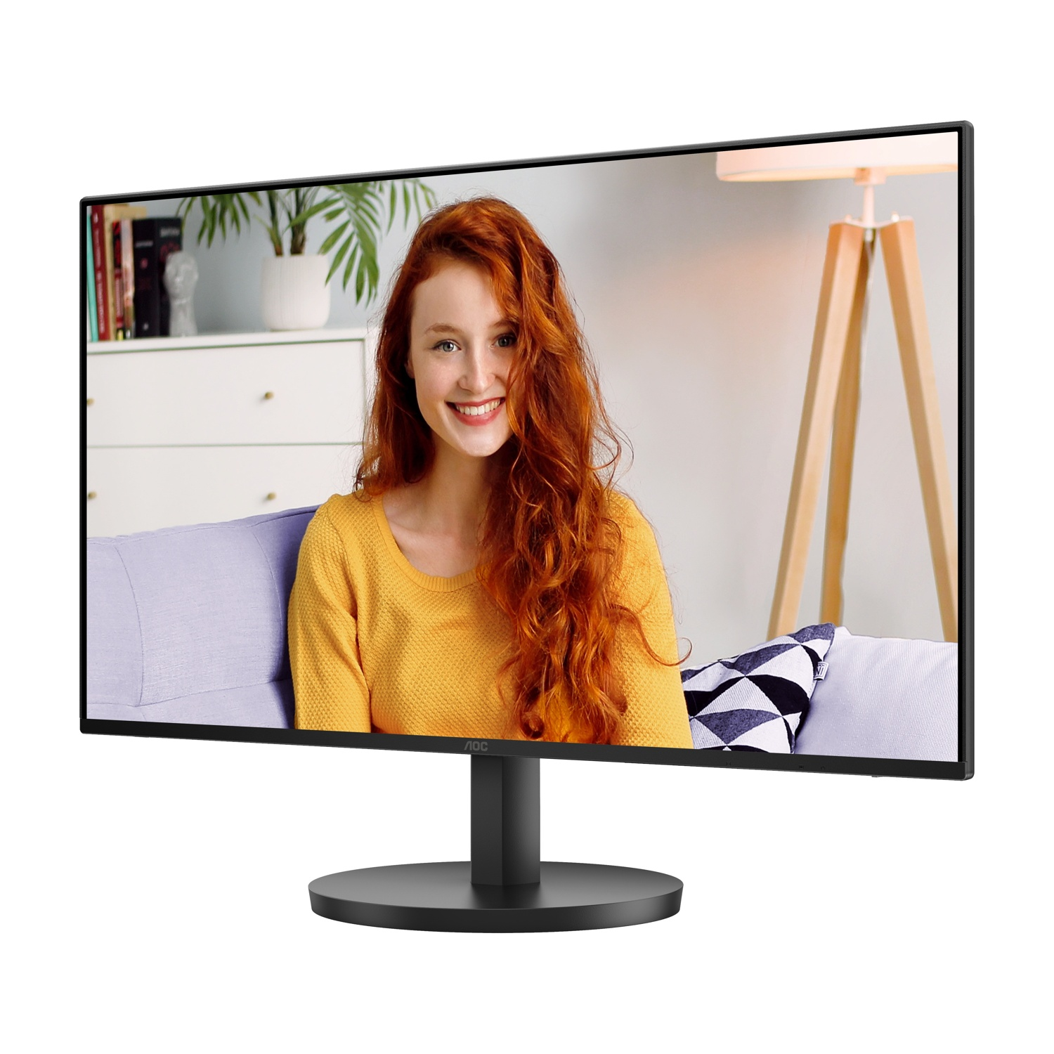 Monitor mostra donna con capelli rossi, maglione giallo, sorridente. Sfondo: divano, pianta e lampada in legno.