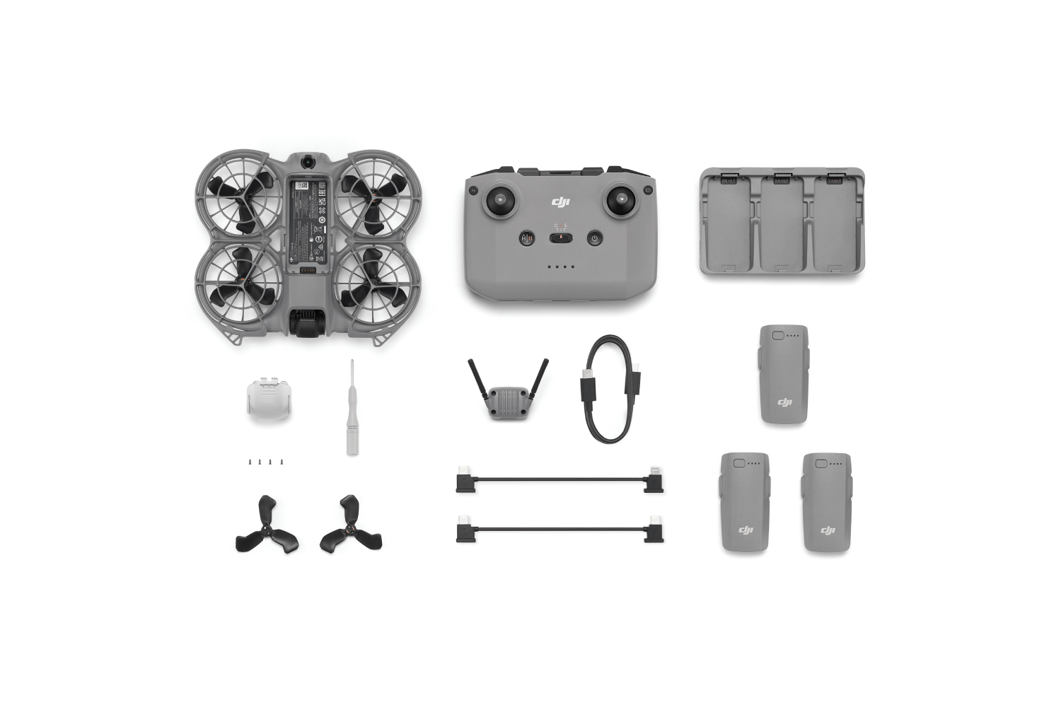 Un kit de drones sobre blanco. Incluye dron, mando, baterías, cargador, cables y herramientas. Componentes grises y negros.