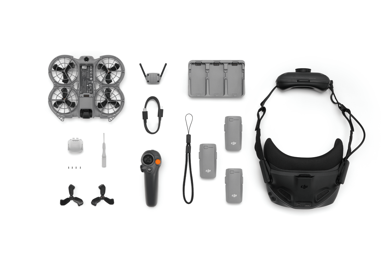Kit de dron con dron, gafas, mando a distancia, cargador, baterías, cables y accesorios, todo sobre fondo blanco.