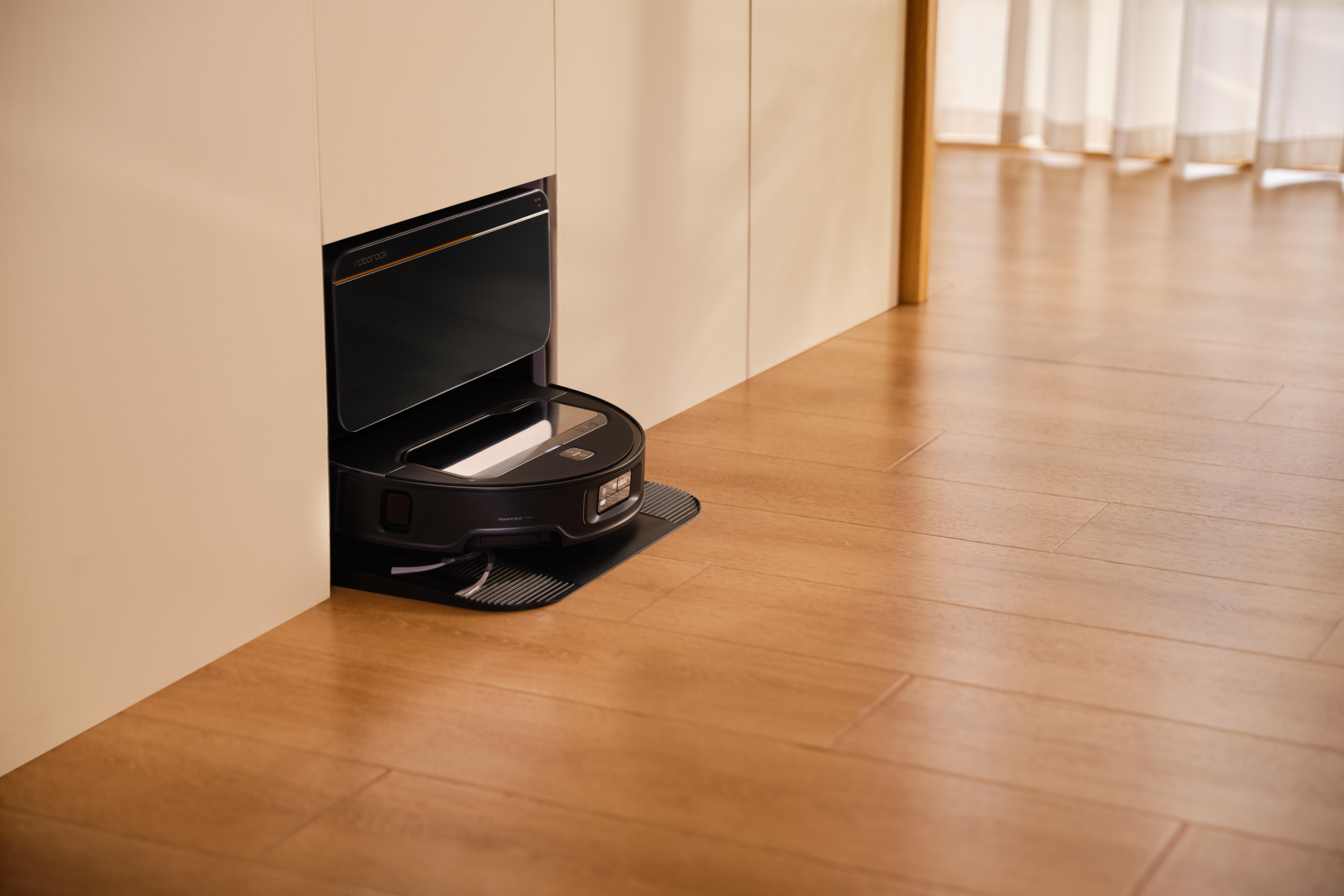 Ein schwarzer Roboter-Staubsauger steht teilweise in einem Schrank. Holzboden und ein Türrahmen mit Vorhängen im Hintergrund.