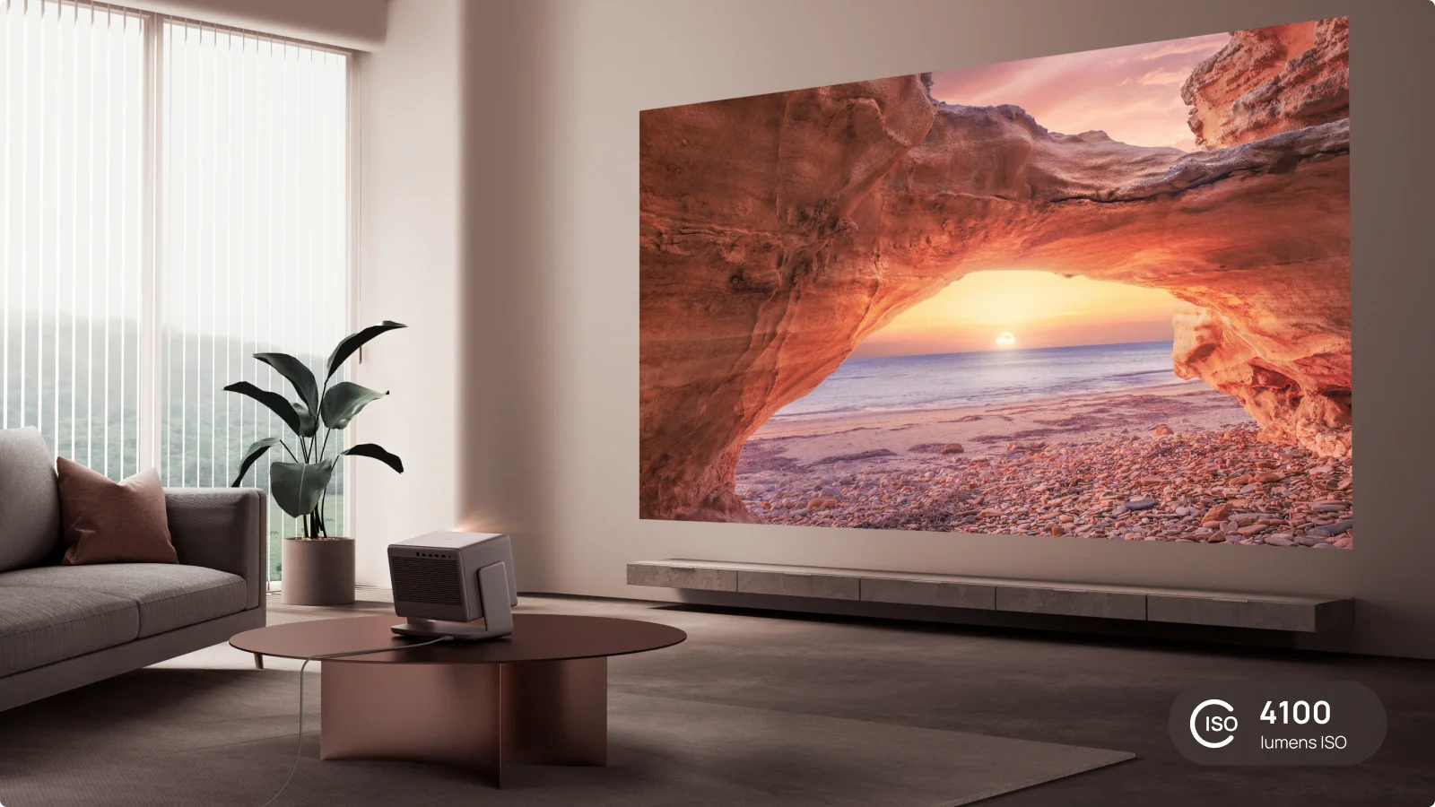Wohnzimmer mit projiziertem Strand. Mit Sofa, Pflanze und Projektor. Die Szene zeigt einen Sonnenuntergang durch einen Felsbogen.