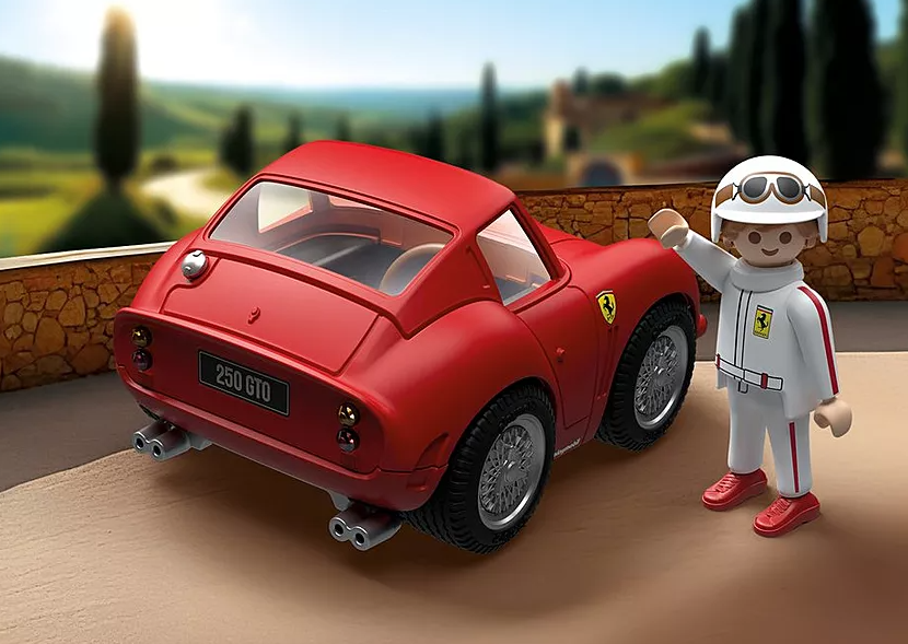 Roter Ferrari-Spielzeugwagen mit winkender Rennfahrerfigur. Der Hintergrund zeigt eine verschwommene Landschaft mit grünen Hügeln.