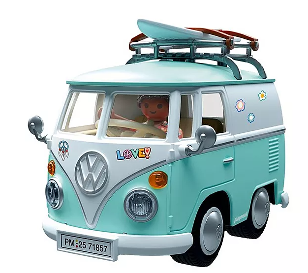 Ein Spielzeug-VW-Bus, türkis und weiß, mit Surfbrett oben. Eine Puppe fährt. Dekoriert mit Friedenssymbolen.