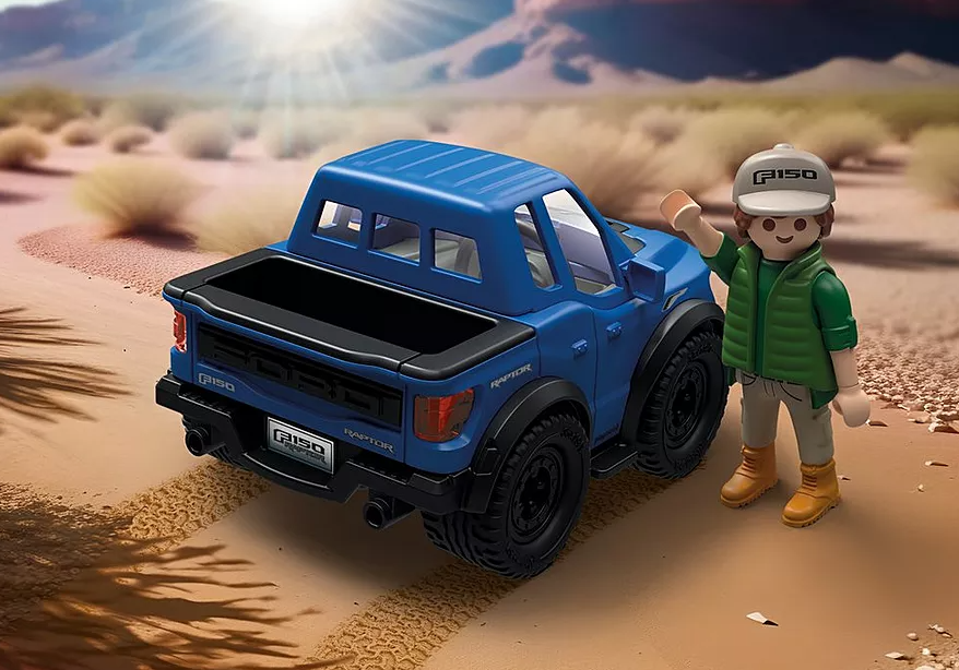 Ein blauer Spielzeug-Ford F-150 Raptor-Truck mit winkender Figur, in einer Wüstenlandschaft mit hellem Hintergrund.