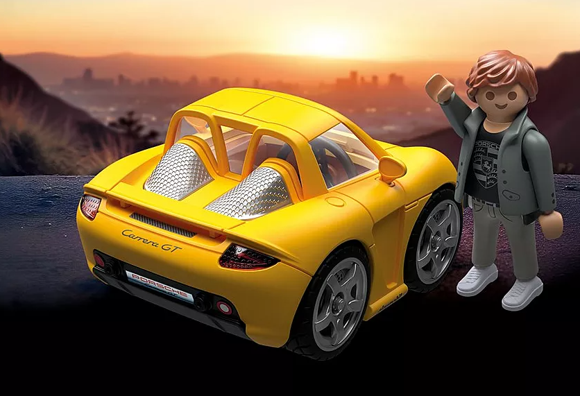 Ein gelber Spielzeug-Porsche Carrera GT mit winkender Figur, vor einer Kulisse einer Sonnenuntergangs-Stadt.