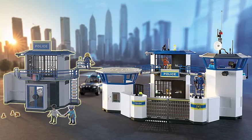 Eine Spielzeug-Polizeistation mit Figuren. Enthält einen Hubschrauberlandeplatz, ein Polizeiauto und mehrere Polizisten. Gebäude haben blaue Akzente.