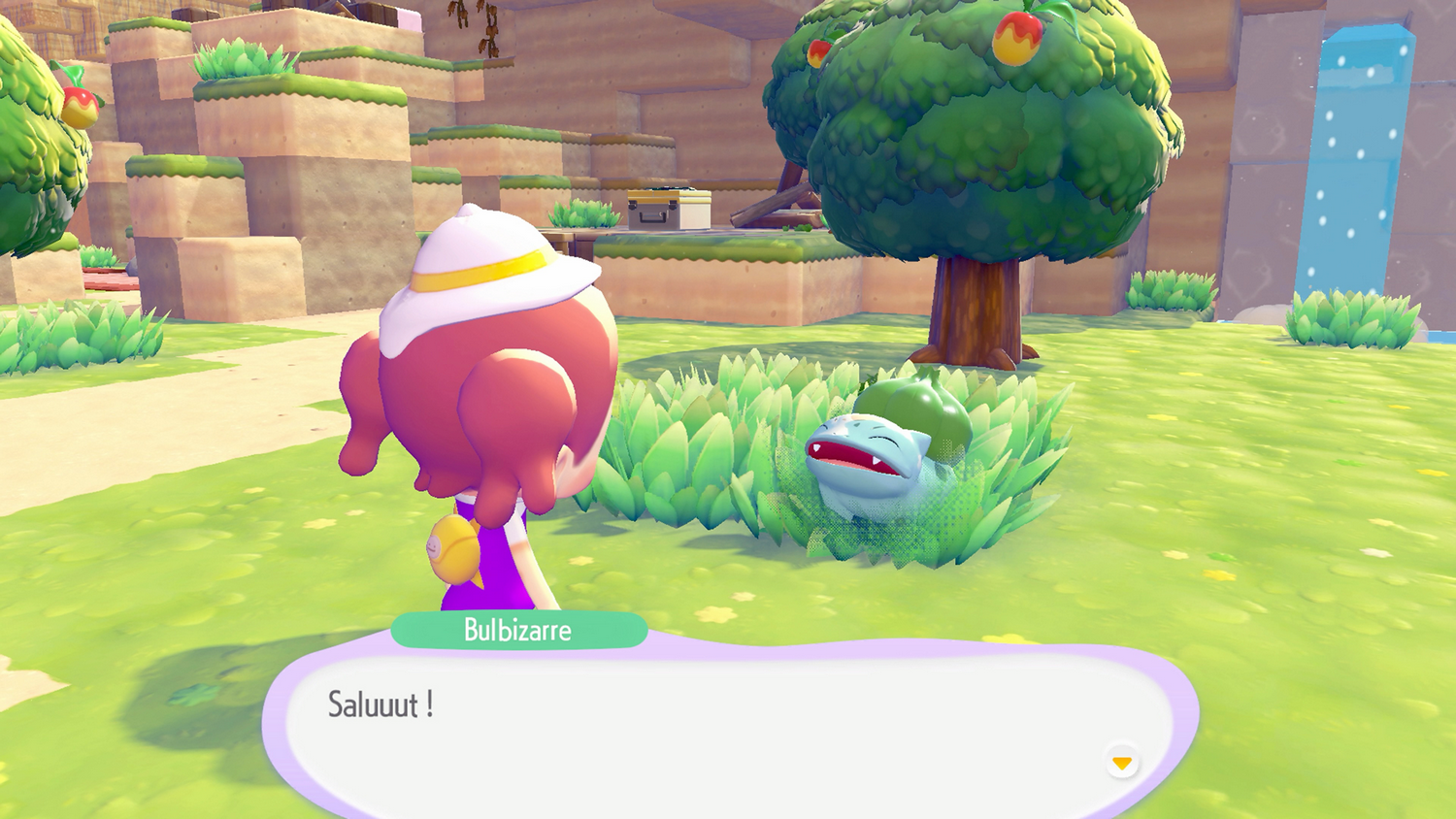 Un personaje con sombrero blanco mira a un Bulbasaur en la hierba. Un bocadillo dice 'Saluuut!'. El fondo muestra árboles y colinas.