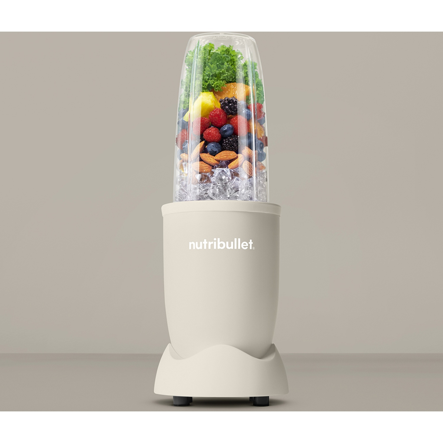 A blender filled with fruits, nuts, and ice. The blender is cream-colored, with the word 'nutribullet' on it.