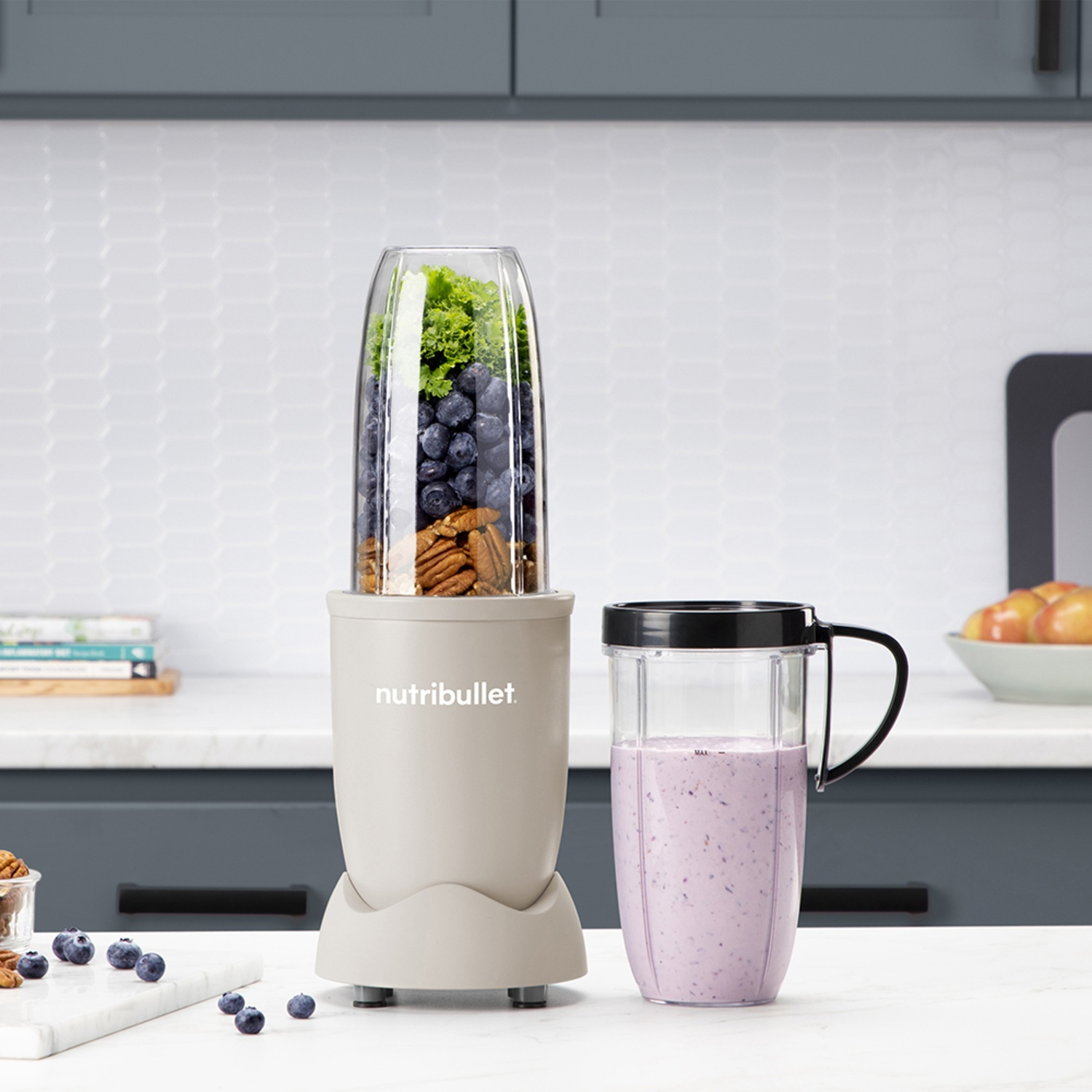 A Nutribullet with ingredients: blueberries, pecans, and kale. A filled cup with a smoothie. Blueberries are scattered around.