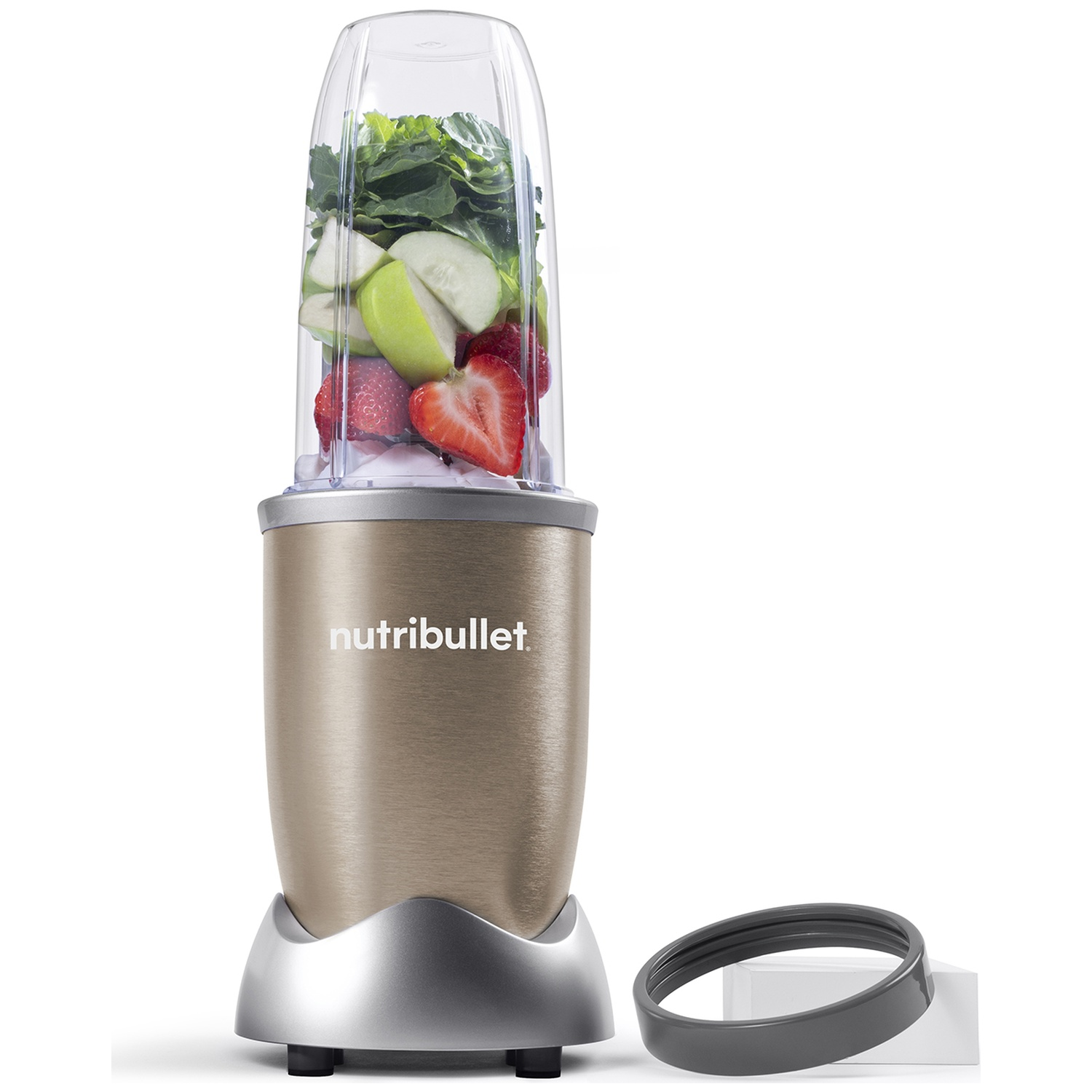 A Nutribullet blender with fruits and vegetables inside. Strawberries, apple slices, and greens are visible. A grey ring sits next to it.