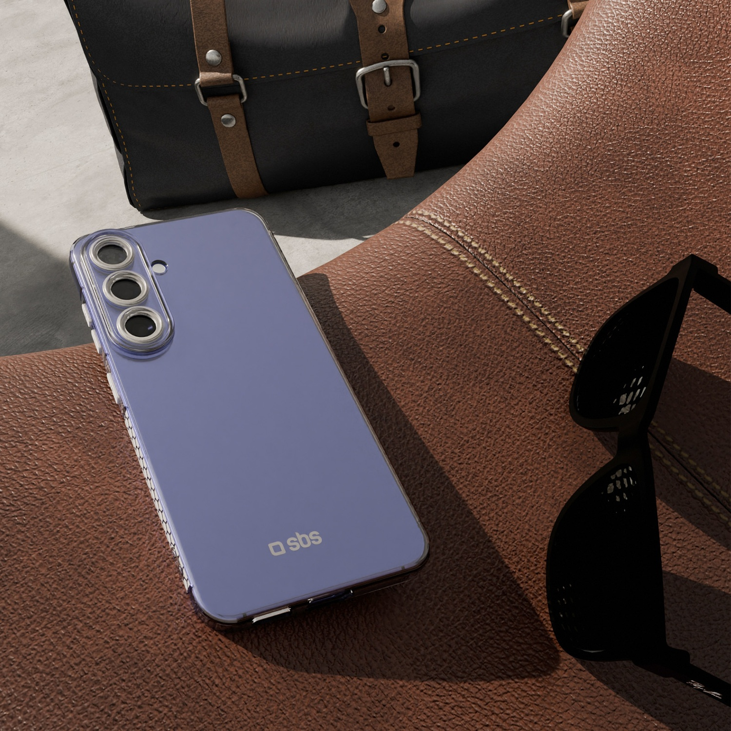 Un téléphone violet avec un étui repose sur une surface en cuir marron à côté de lunettes de soleil. Un sac noir est en arrière-plan.