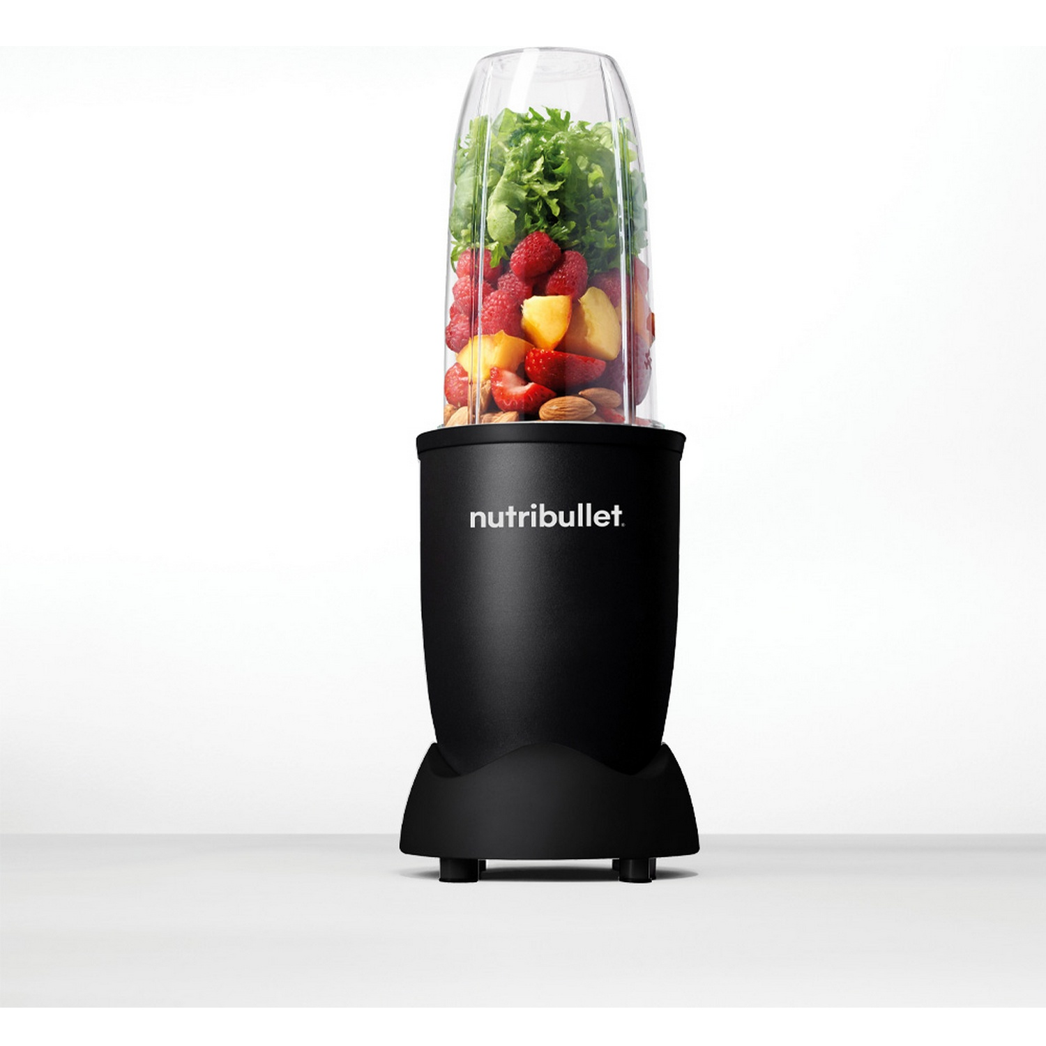 Een zwarte Nutribullet blender gevuld met fruit en groenten. Frambozen, perziken, amandelen en bladgroenten zijn zichtbaar.