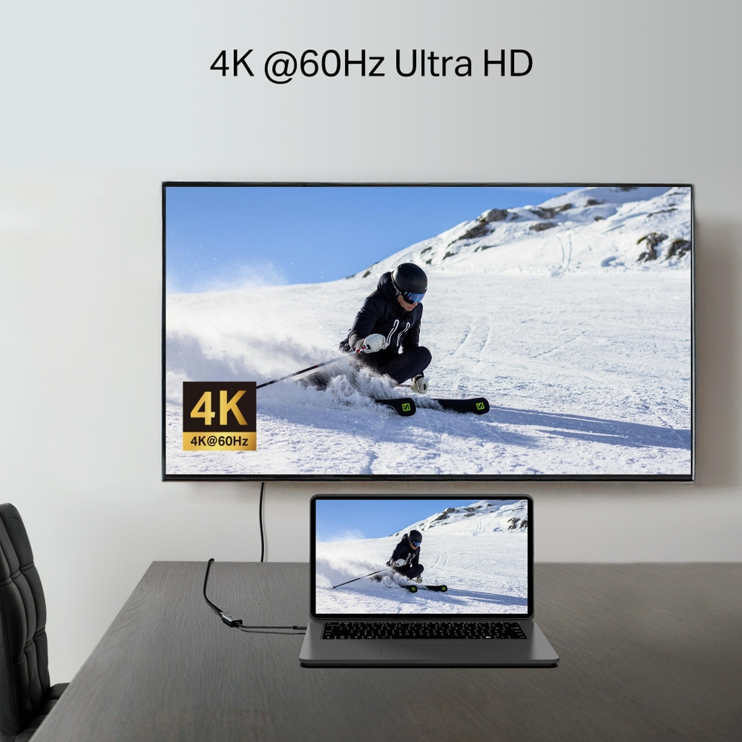 Une télévision et un ordinateur portable affichent un skieur. Un câble les relie. Une chaise noire à gauche. La scène est sur une table.