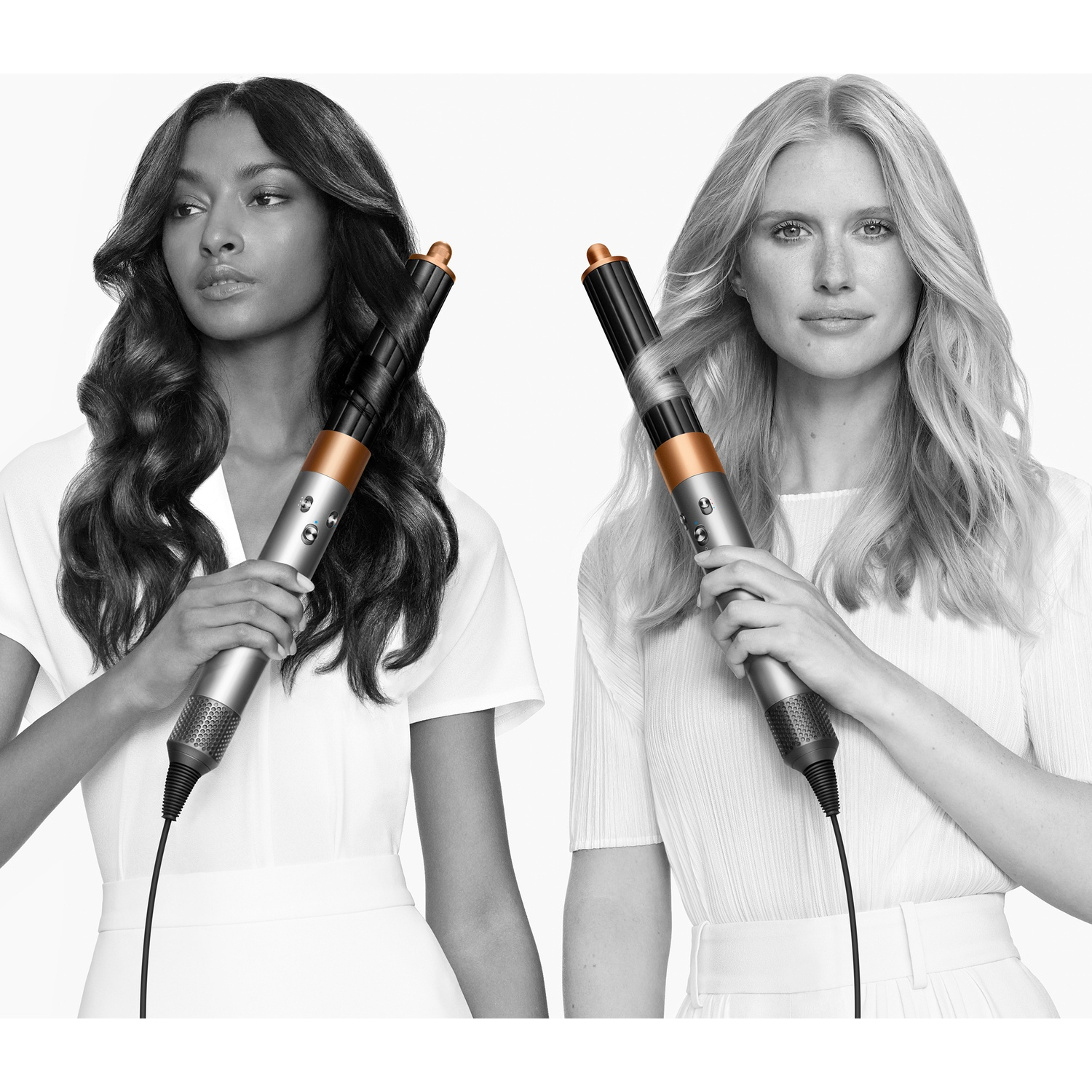 Two women holding hair stylers. One has dark hair and the other blonde, both in white dresses, against a white backdrop.