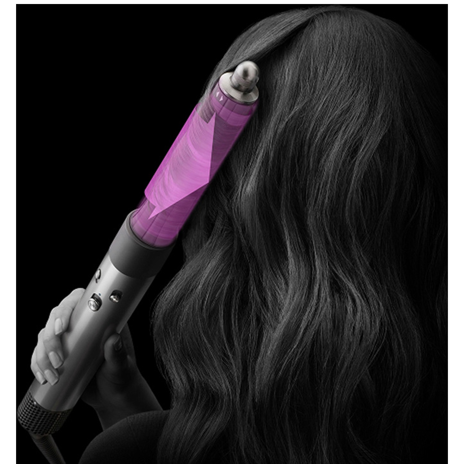 A person using a silver hair styler with a pink barrel on dark wavy hair against a black background.